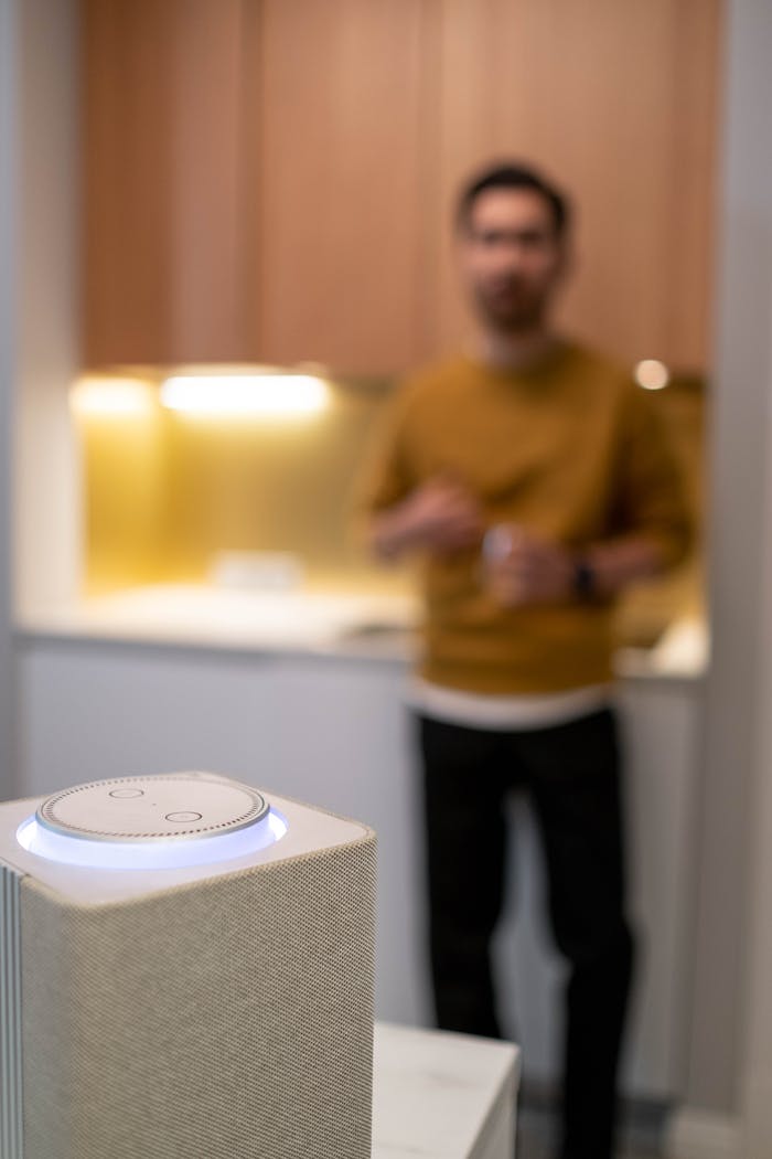 journey-01 Blurred man commands a wireless smart speaker in a contemporary kitchen setting.